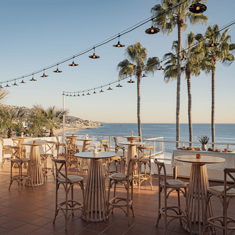 A relaxed rooftop bar setting with rattan seating, warm lighting, and panoramic ocean views.